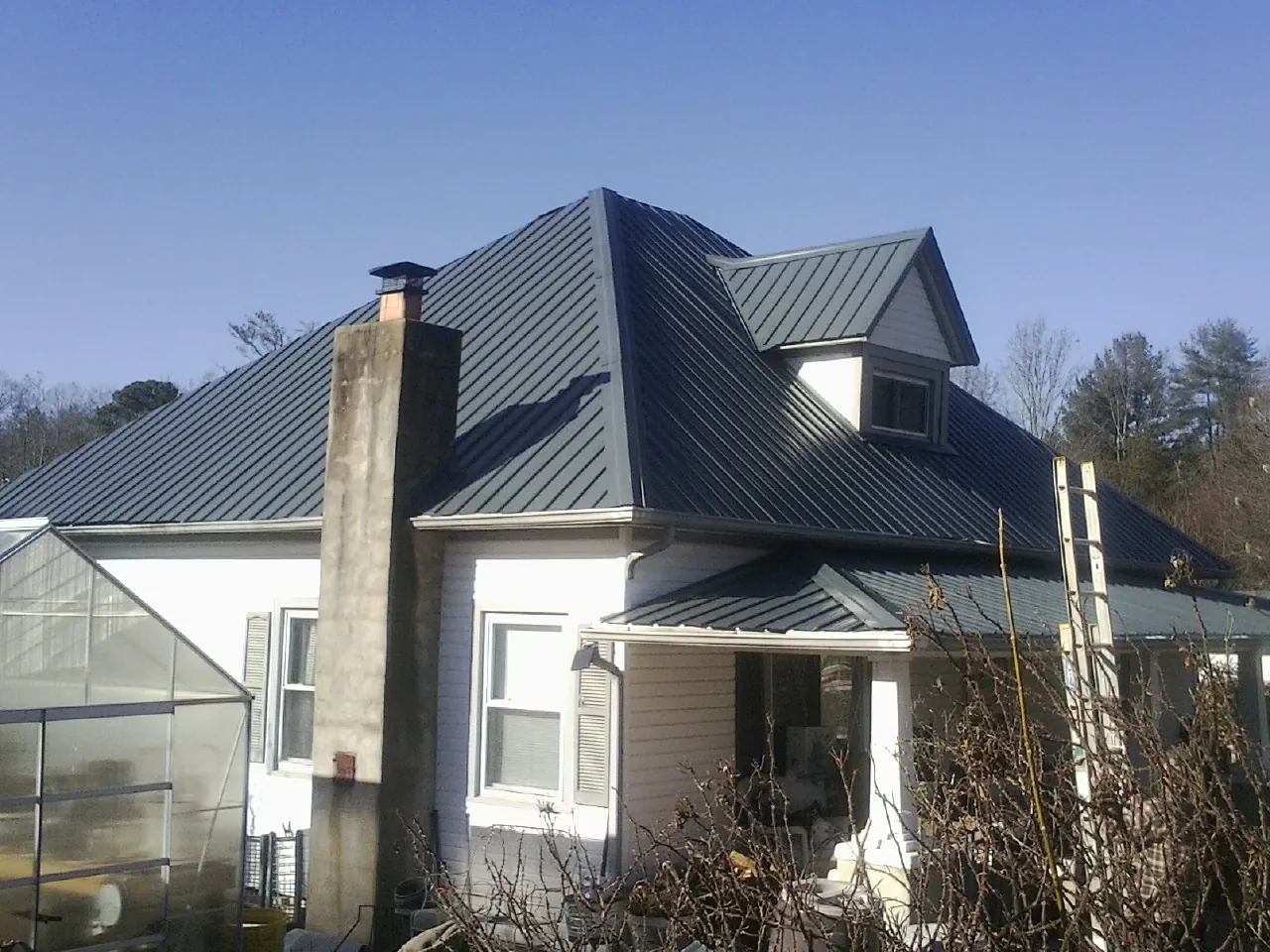 Dark blue standing seam metal roof on a white farmhouse with dormer — Slate & Tile Roof Repair by Roofing Brothers in Mount Dora