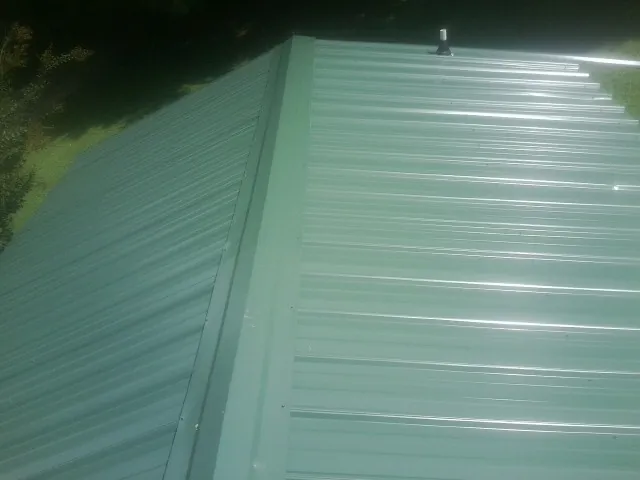 New green metal panels meeting at the ridge of a roof — Flat Roof Repair work by our crew in Mount Dora