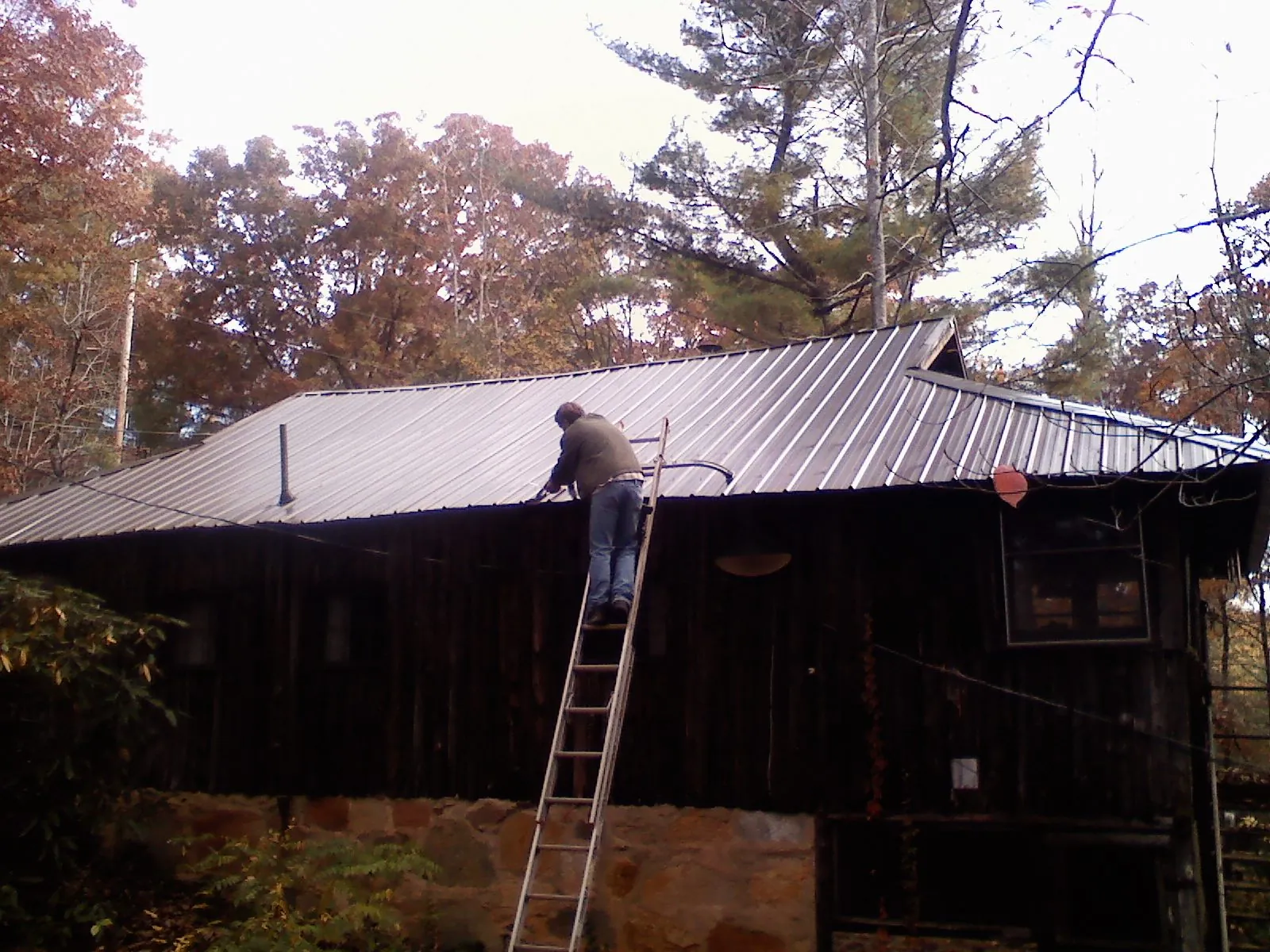 Roofer on a ladder working along the edge of a cabin metal roof in Mount Dora
