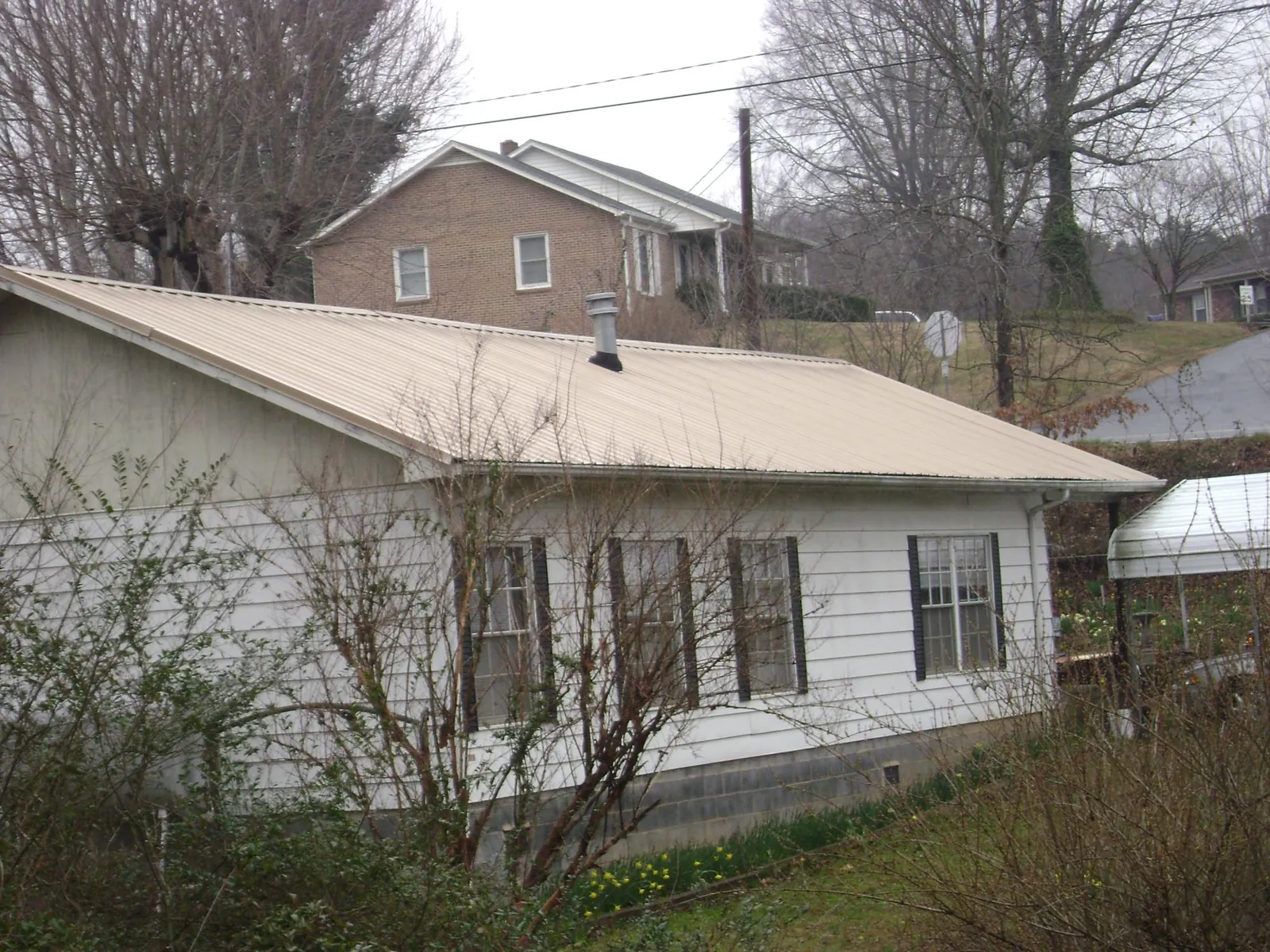 Tan metal roof on a white sided house set into a hillside — Commercial Roofing by Roofing Brothers in Mount Dora